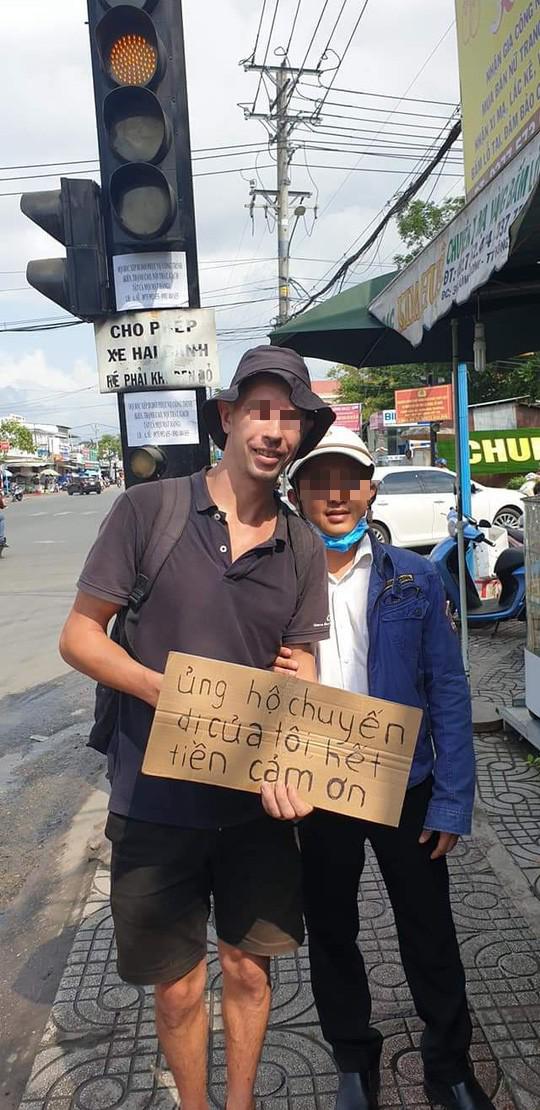 Một người đàn ông nước ngoài đeo bảng xin tiền, đứng kế bên có thể là người đàn ông Việt Nam