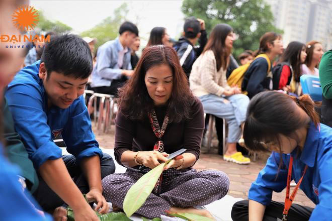 Bà Cao Thị Hòa cẩn thận cắt tỉa từng chiếc lá bàng vuông, hướng dẫn sinh viên gói bánh.