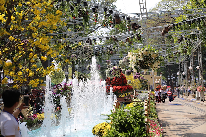  Ngay cổng vào Hội hoa Xuân ở mặt đường Trương Định là đường hoa rực rỡ với đài phun nước. Đặc biệt phá cách so với mọi năm, những chùm hoa treo trên cao liên tục được kéo lên hạ xuống bởi hệ thống ròng rọc tự động.