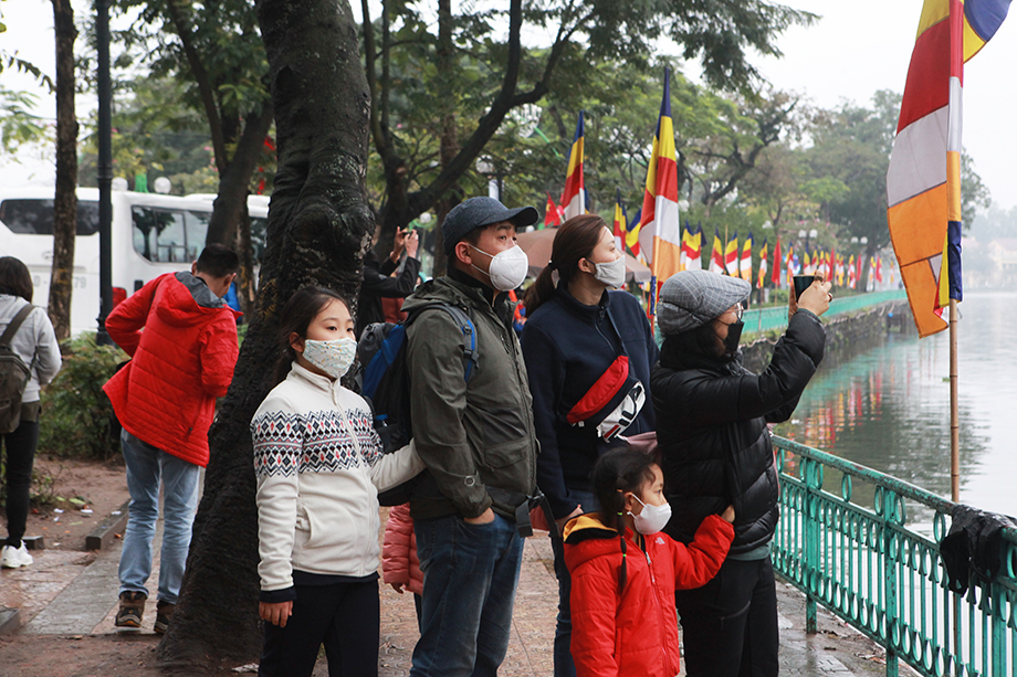 Một nhóm du khách nước ngoài đứng bên ngoài vỉa hè đường Thanh Niên ngắm chùa, chụp ảnh. Hầu hết du khách đều đeo khẩu trang để phòng dịch virus Corona.