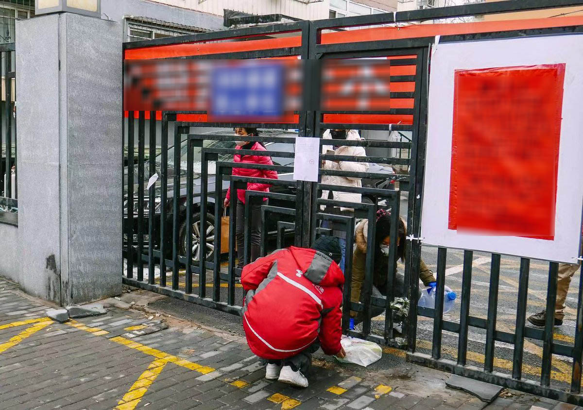 Một nhân viên giao hàng đưa đồ tới cho người phụ nữ qua cánh cổng bị khóa ở thủ đô Bắc Kinh. Ảnh: Thời báo Hoàn cầu