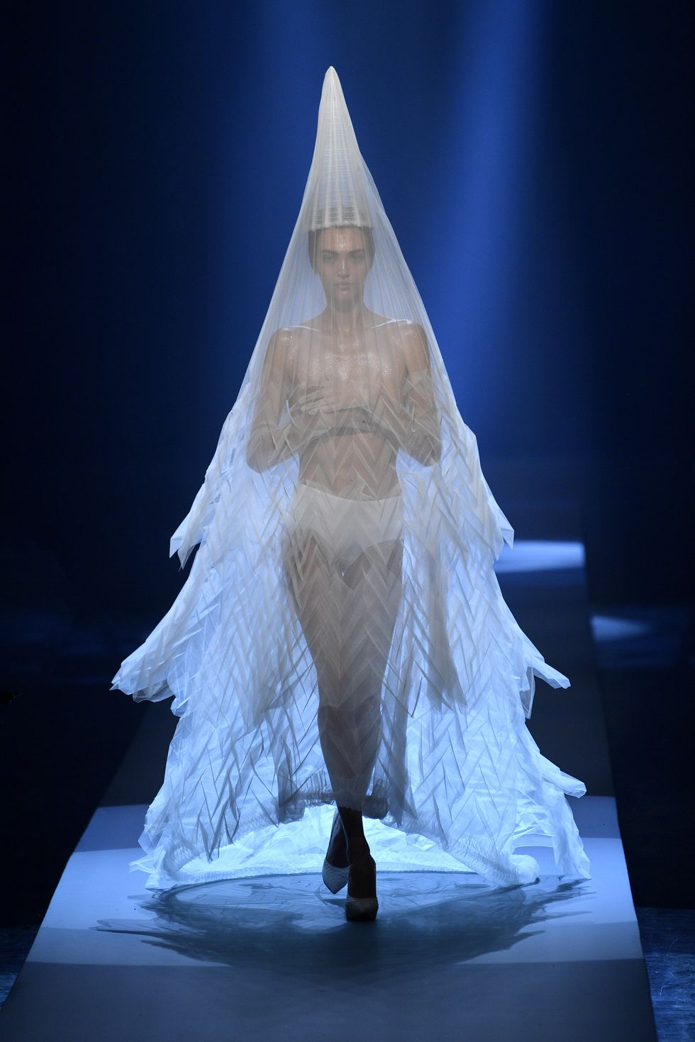Đối với
trang phục cô dâu hình nón này, Gaultier đã tôn vinh một số họa
tiết phổ biến anh sử dụng trong suốt sự nghiệp của mình, chẳng hạn
như hình dạng nhọn, góc cạnh và nhiều chi tiết khơi gợi sự hấp dẫn
giới tính. Trang phục nằm trong BST Haute Couture 2019.
