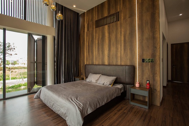 Phòng ngủ được thiết kế trần khá cao giúp không gian đã thoáng càng thoáng hơn. Nội thất tối giản, nổi bật với bức tường ốp gạch giả gỗ ton-sur-ton.
