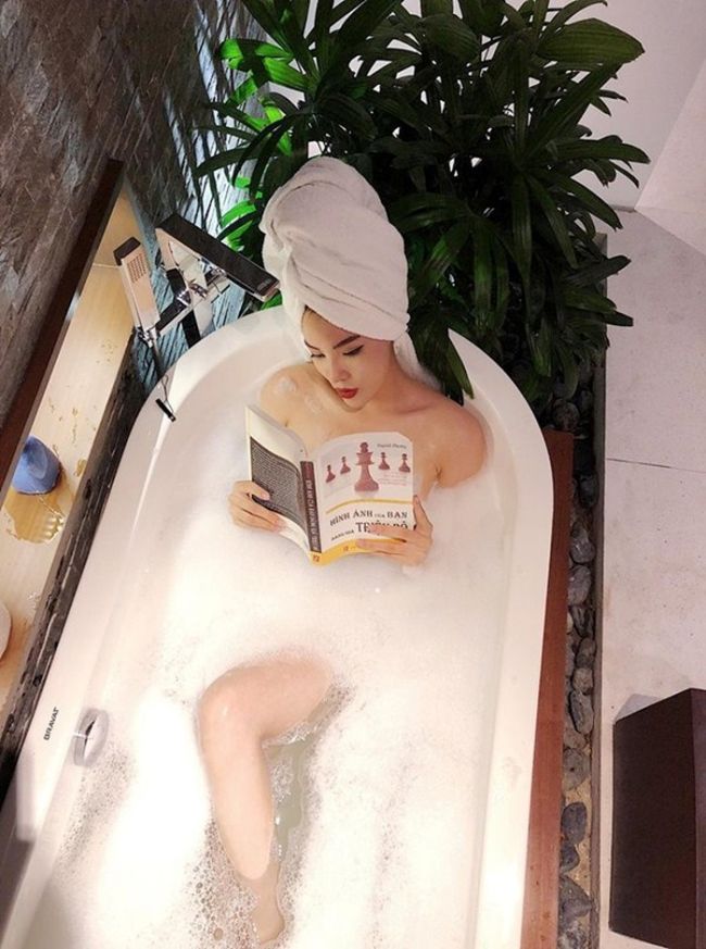 Hoa hậu Kỳ Duyên khéo léo dùng sách che vòng 1 khi tạo dáng ở bồn tắm.
