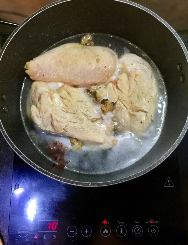 Ức gà được luộc bằng nước lạnh, cho thêm 2 thìa gia vị và hành khô cùng gừng nướng cho thơm