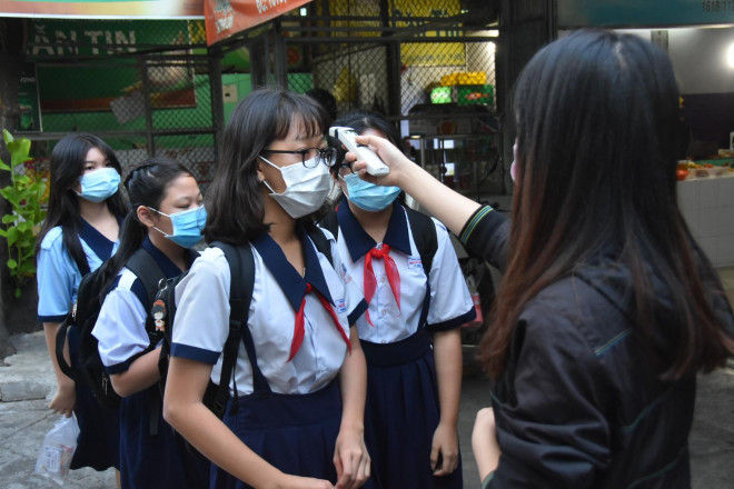 Học sinh xếp hàng để giáo viên đo thân nhiệt