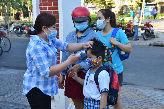 Cô giáo đo thân nhiệt cho trẻ trước khi nhận các em từ phụ huynh để đưa vào lớp