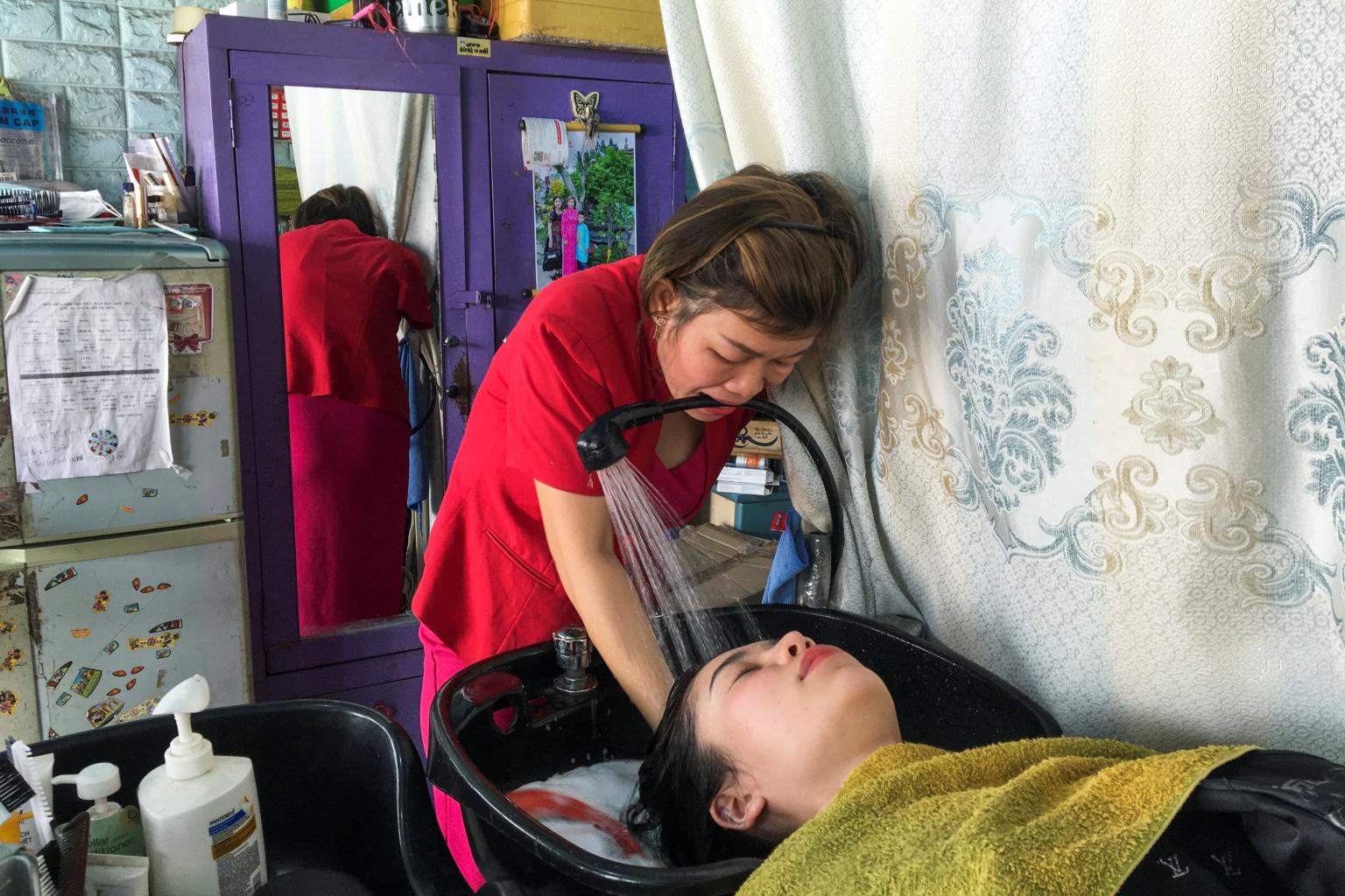 Bà Trâm gội đầu cho khách chỉ với một tay. Ảnh: Reuters