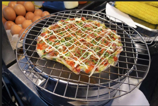 Dọc các con đường vào chợ đêm Phú Quốc không khó bắt gặp những xe bánh tráng nướng. Bánh tráng nướng thơm lừng thêm chút vị béo của trứng, phô mai, vị cay cay của tương ớt và rắc dăm bông đậm đà lên tạo nên món ăn vặt ngon và bùi. 