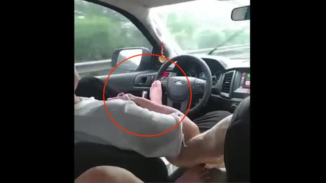 Tài xế nắm tay cô gái bên cạnh, dùng chân điều khiển ô tô khi trời đang mưa.