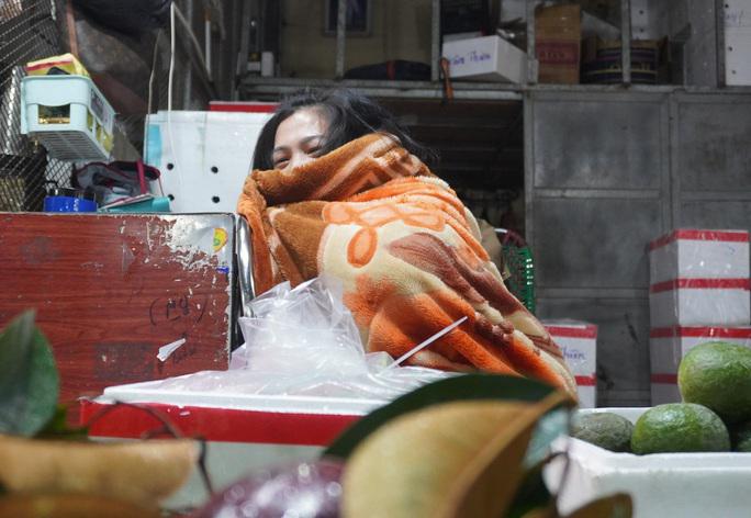 Chủ một ki-ốt choàng chăn kín mít để chống chọi lại với cái lạnh xuyên đêm ở chợ đầu mối