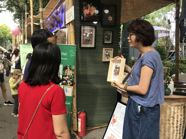 Chị Mây giới thiệu các sản phẩm làm từ hoa giấy cho khách hàng tại một hội chợ ở Hà Nội.