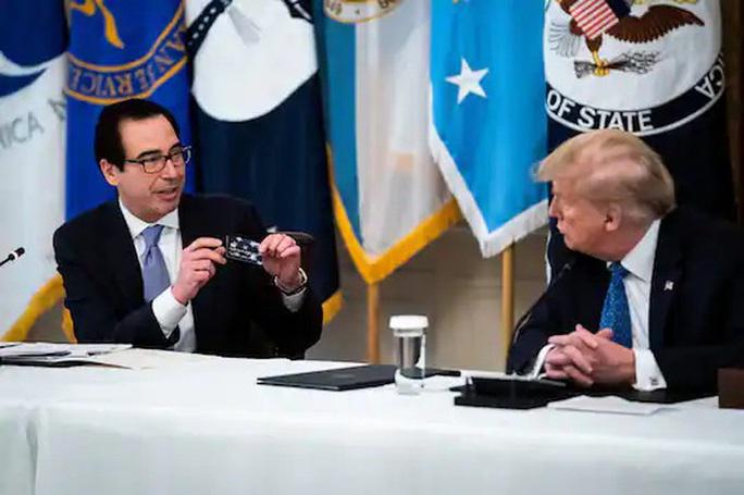 Cựu Bộ trưởng Tài chính Mỹ, ông Steven Mnuchin, giơ lên cho cựu Tổng thống Donald Trump xem một chiếc thẻ được dùng để gửi tiền hỗ trợ cho người Mỹ trong một cuộc họp nội các tại Nhà Trắng hồi tháng 5-2020. Ảnh: The Washington Post