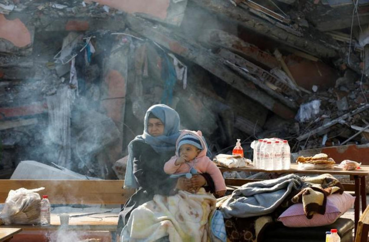 Mẹ bồng&nbsp;con co ro trong giá rét cạnh một tòa nhà bị sập ở Hatay, Thổ Nhĩ Kỳ vào ngày 10-2. Ảnh: Umit Bektas/REUTERS