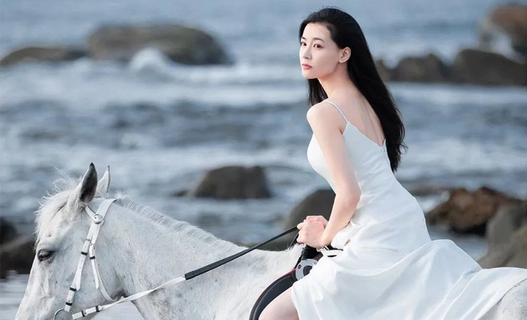 Người đẹp Trung Quốc mặc váy lụa chụp ảnh với ngựa bên bờ biển.
