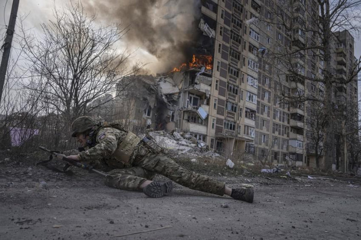 Một cảnh sát Ukraine nấp trước một tòa nhà đang bốc cháy do bị trúng bom trong một cuộc không kích ở thị trấn Avdiivka, tỉnh Donetsk, vùng Donbass (miền Đông Ukraine), vào ngày 17-3. Ảnh: AP