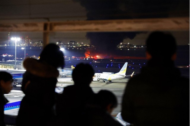 Người dân đứng nhìn chiếc máy bay Japan Airlines bốc cháy từ một tòa nhà ở sân bay Haneda ở Tokyo vào ngày 2-1. Ảnh: Kyodo