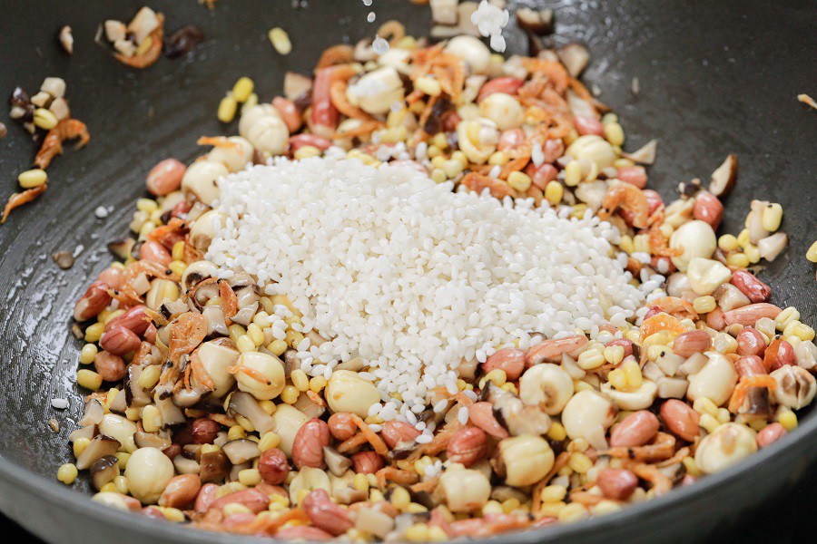 Tiếp tục cho đậu xanh, hạt sen và đậu phộng vào xào. Sau đó cho gạo nếp vào đảo đều.