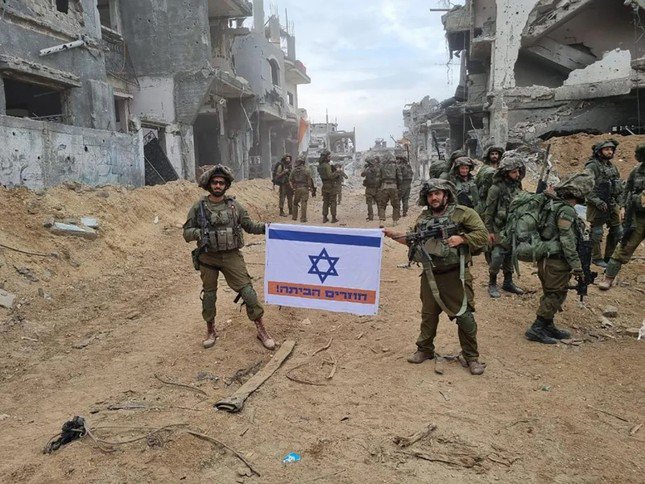 Hai người lính Israel ở Dải Gaza cầm một lá cờ Israel, được thay đổi để bao gồm một sọc màu cam và dòng chữ bằng tiếng Do Thái “Về nhà!”Ảnh: CNN