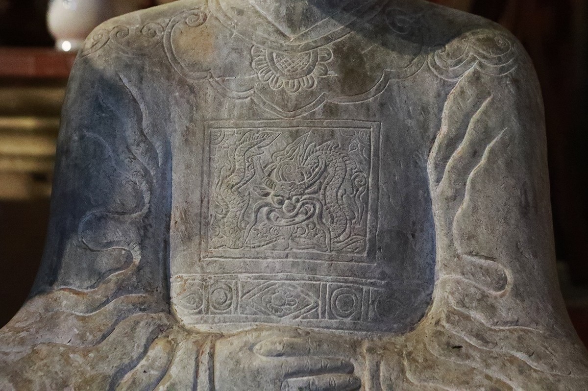 Trên áo có chạm hình rồng trong thế cuộn tròn, mang đặc trưng rồng thời Mạc.