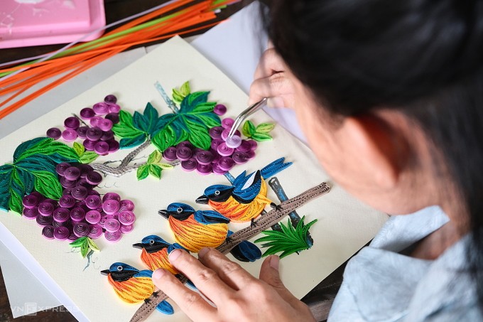 Chị Hồ Thi Lắng xếp chồng các chi tiết tạo hình từ giấy xoắn cho bức tranh đàn chim và chùm nho. Ảnh: Nguyễn Đông