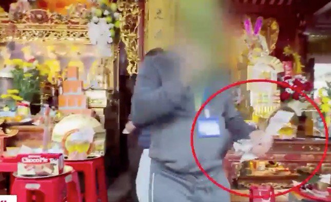 Hình ảnh cắt từ clip ghi lại cảnh cán bộ Ban quản lý đền thu gom tiền khách để trên các ban thờ nhưng lại bỏ vào vỏ hộp bánh.