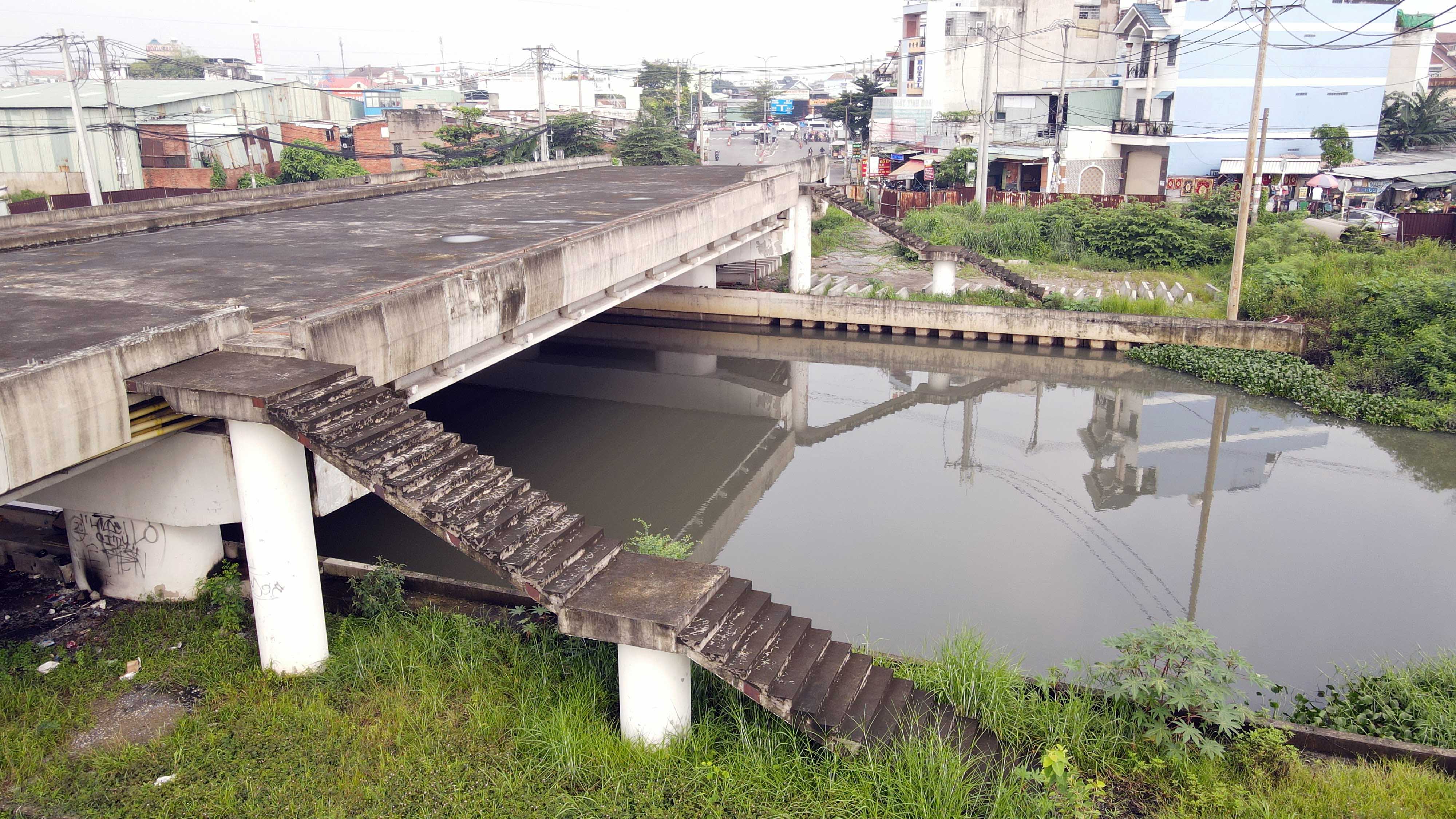  Hiện tại, bên trong công trình xây dựng cầu không có công nhân, cỏ dại mọc um tùm, vật liệu nằm ngổn ngang. Nhiều hạng mục bỏ không thi công lâu ngày nên có dấu hiệu xuống cấp. Các thang dẫn bộ lên cầu đã xong nhưng đã ố đen, bong tróc.