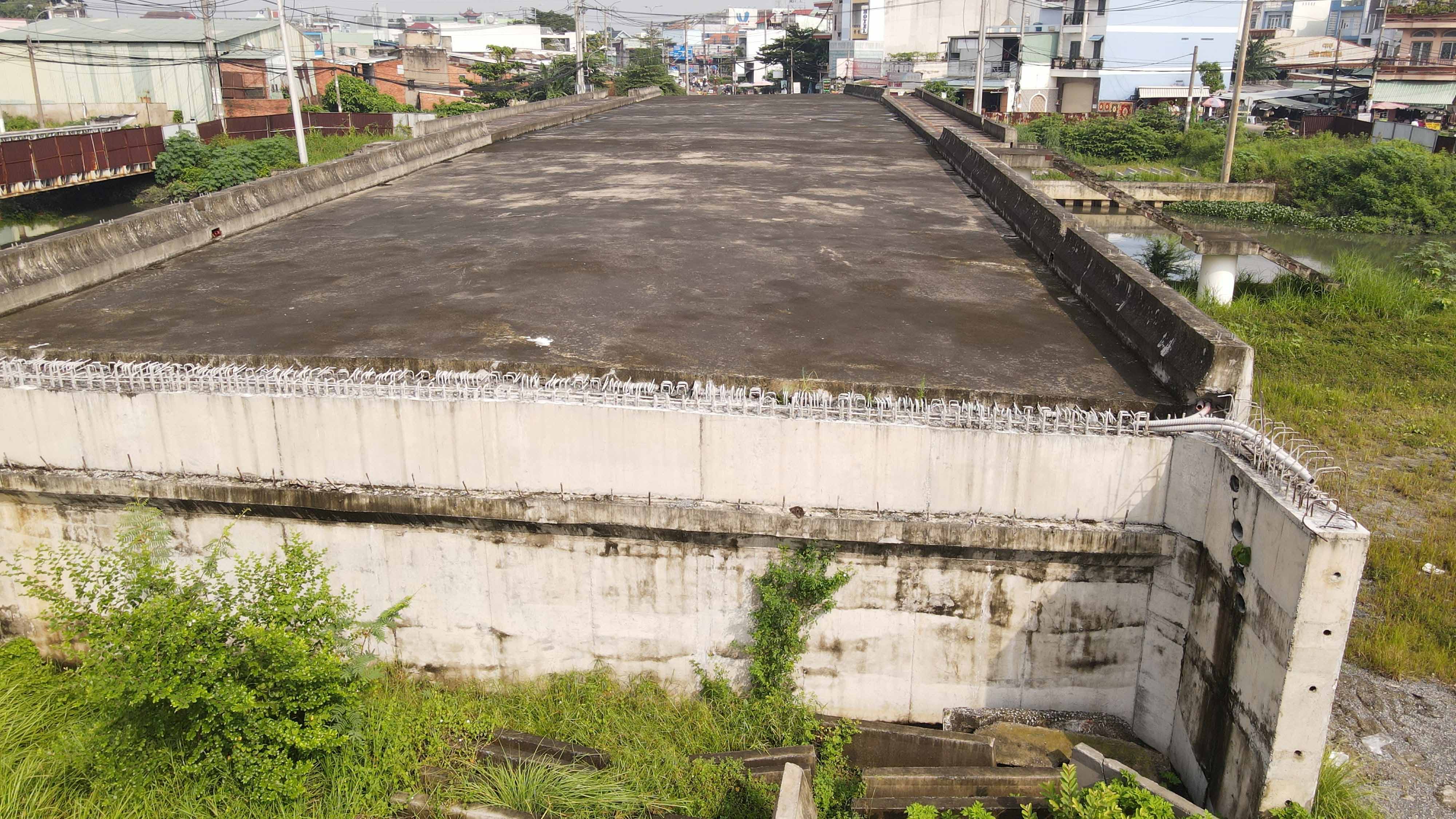  Hàng rào tôn cao 2m bao quanh công trình nhiều đoạn ố vàng, dán chằng chịt các tờ rơi quảng cáo...Phần cầu xây bắc qua kênh có nhiều đoạn bê tông lồi lõm, sắt thép ngổn ngang, gỉ sét do phơi nắng mưa lâu ngày.