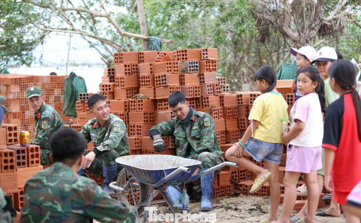 Trong những phút nghỉ ngơi sau giờ lao động vất vả, các chiến sĩ bộ đội quây quần trò chuyện cùng các em nhỏ ở xóm Cồn Chim, mang đến không khí ấm áp, gần gũi, xua tan phần nào những nhọc nhằn giữa vùng sóng nước còn nhiều gian khó. Ảnh: Trương Định