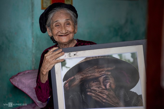 Cụ Xong bên tác phẩm "Nụ cười ẩn giấu" của nhiếp ảnh gia Rehahn. Ảnh: Nguyễn Đông