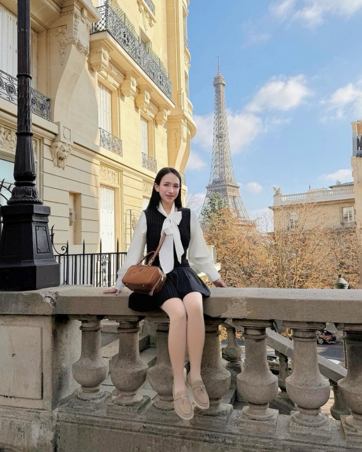 Con gái Minh 'Nhựa' diện đồ phong cách preppy với váy yếm và sơ mi cổ nơ, kết hợp túi xách Miu Miu cùng giày loafer Lori Piana khi chụp hình ở Paris.