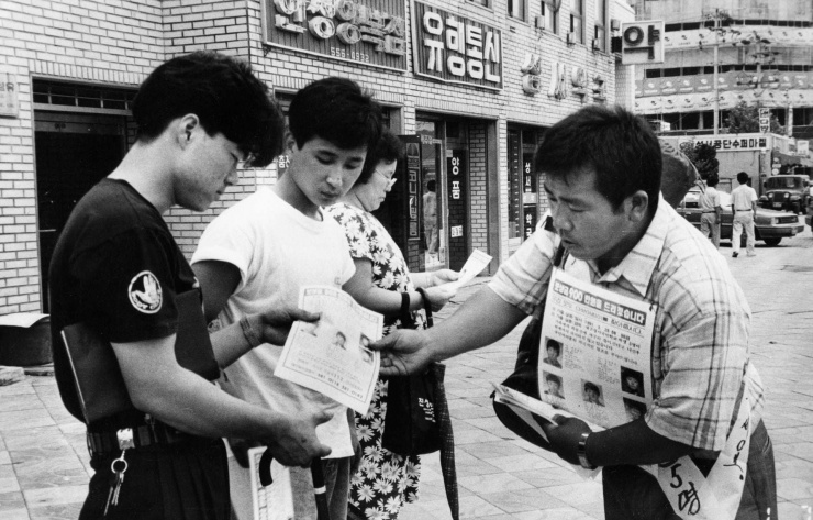 Trong một bức ảnh không rõ ngày tháng, cha của Kim Jong Sik (bên phải) đang phát tờ rơi về vụ mất tích "Những cậu bé ếch" cho người qua đường. (Nguồn: JOONGANG ILBO)