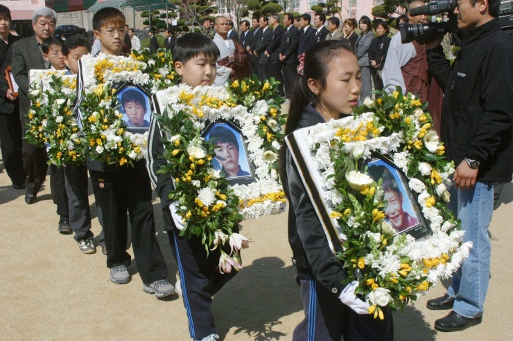 Các học sinh trường tiểu học Seongseo ở Daegu cầm ảnh của các "Cậu bé ếch" trong buổi lễ tưởng niệm chung vào ngày 26/3/2004. (Nguồn: CHO MUN-GYU)