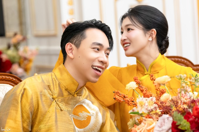 Á hậu diện áo dài lụa thêu hoa sen tông vàng đồng điệu với áo dài thêu họa tiết mặt trời, đỉnh núi tôn vẻ mạnh mẽ của chú rể. Suốt buổi lễ, cặp thường xuyên dành cho nhau những cử chỉ tình tứ, ngọt ngào.