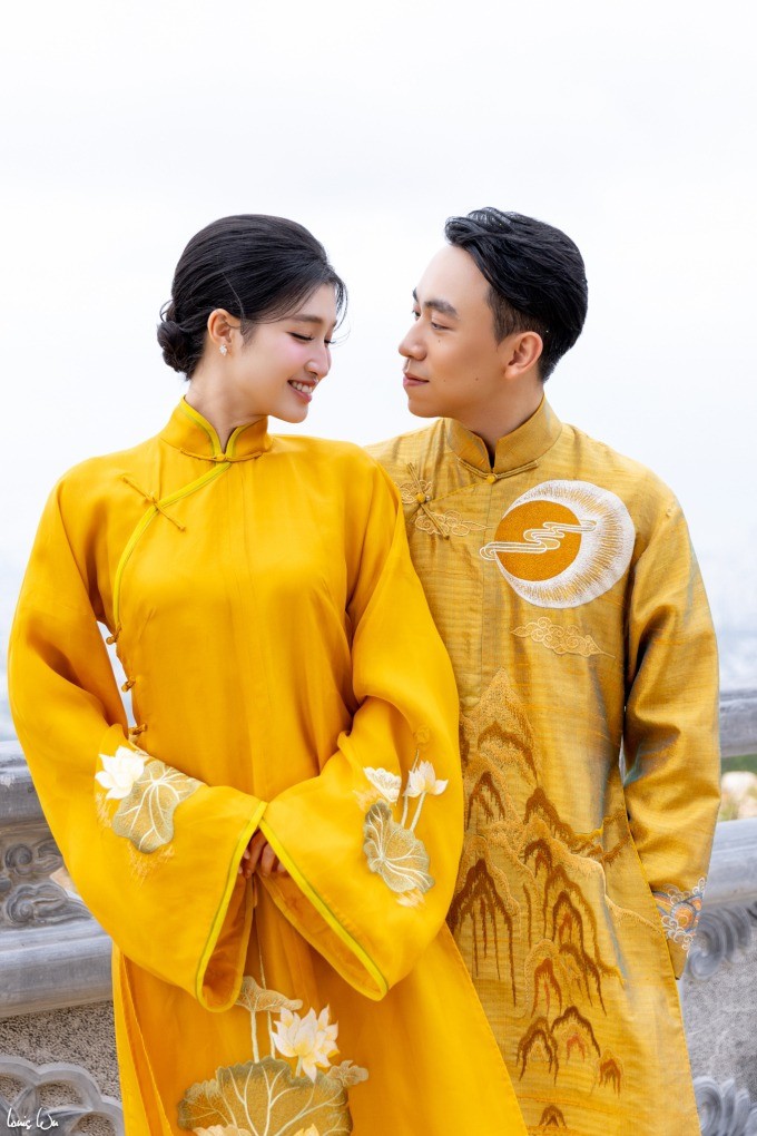 Phương Nhi diện chiếc áo dài phom dáng cổ điển làm từ chất liệu tơ tằm quý hiếm, thân áo thêu thủ công hoa sen thể hiện dáng vẻ tinh khôi, mềm mại. Sánh đôi bên vợ, Minh Hoàng diện áo dài vàng sắc trầm, thêu họa tiết núi non và vầng dương, đại diện cho sự mạnh mẽ, vững chãi.