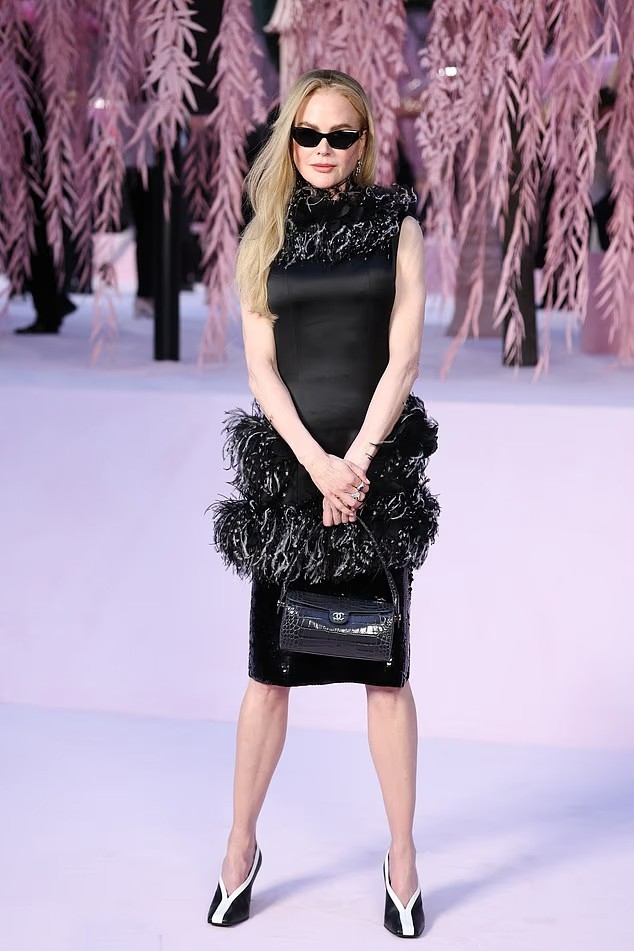 Nicole Kidman là một trong những khách mời nổi bật tại show diễn thời trang cao cấp Xuân/Hè 2026 của Chanel diễn ra ngày 27/1. Minh tinh 58 tuổi gây ấn tượng với diện mạo sành điệu trong chiếc váy đen ôm sát, được điểm xuyết chi tiết lông vũ đen - trắng ở cổ áo và hông. Thiết kế thuộc bộ sưu tập Chanel Métiers d’Art 2026. Nicole hoàn thiện tổng thể bằng đôi giày cá tính, túi xách da cá sấu màu đen và kính râm mắt mèo bản lớn - đều đến từ nhà mốt Pháp. Set đồ tông đen nổi bật trên nền hồng của không gian sự kiện.