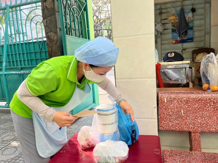 Bảo mẫu Trường Tiểu học Tân Quy nhận cơm từ phụ huynh mang đến cho con, sáng 29/1. Ảnh: Anh Nhàn