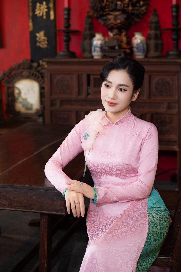 Bộ áo dài màu hồng pastel mềm mại kết hợp hài hòa với phần tà áo xanh ngọc thêu họa tiết tinh xảo mang đến vẻ đẹp thanh lịch, dịu dàng nhưng vẫn rất sang trọng và trang nhã, tôn lên nét duyên dáng, nữ tính đặc trưng của người phụ nữ Việt Nam.