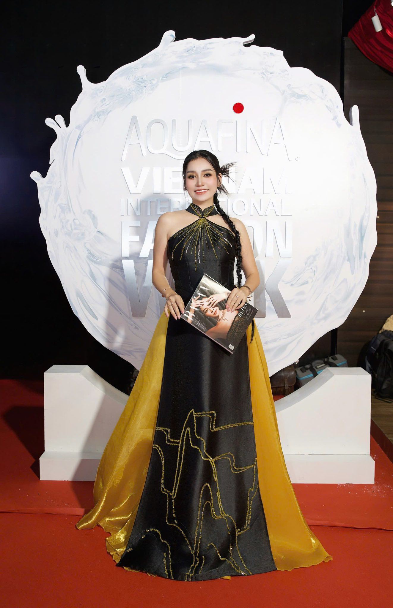 MC Thanh Mai gây ấn tượng khi lựa chọn chiếc áo dài cách tân đầy ấn tượng với gam màu đen chủ đạo kết hợp cùng tà áo vàng rực rỡ, tạo nên sự tương phản hài hòa và cuốn hút. Thiết kế áo dài này không chỉ giữ được nét truyền thống đặc trưng của trang phục Việt Nam mà còn mang phong cách hiện đại với phần cổ yếm độc đáo, điểm nhấn họa tiết ánh kim tinh tế trải dài trên thân áo, thể hiện sự sang trọng và thời thượng.