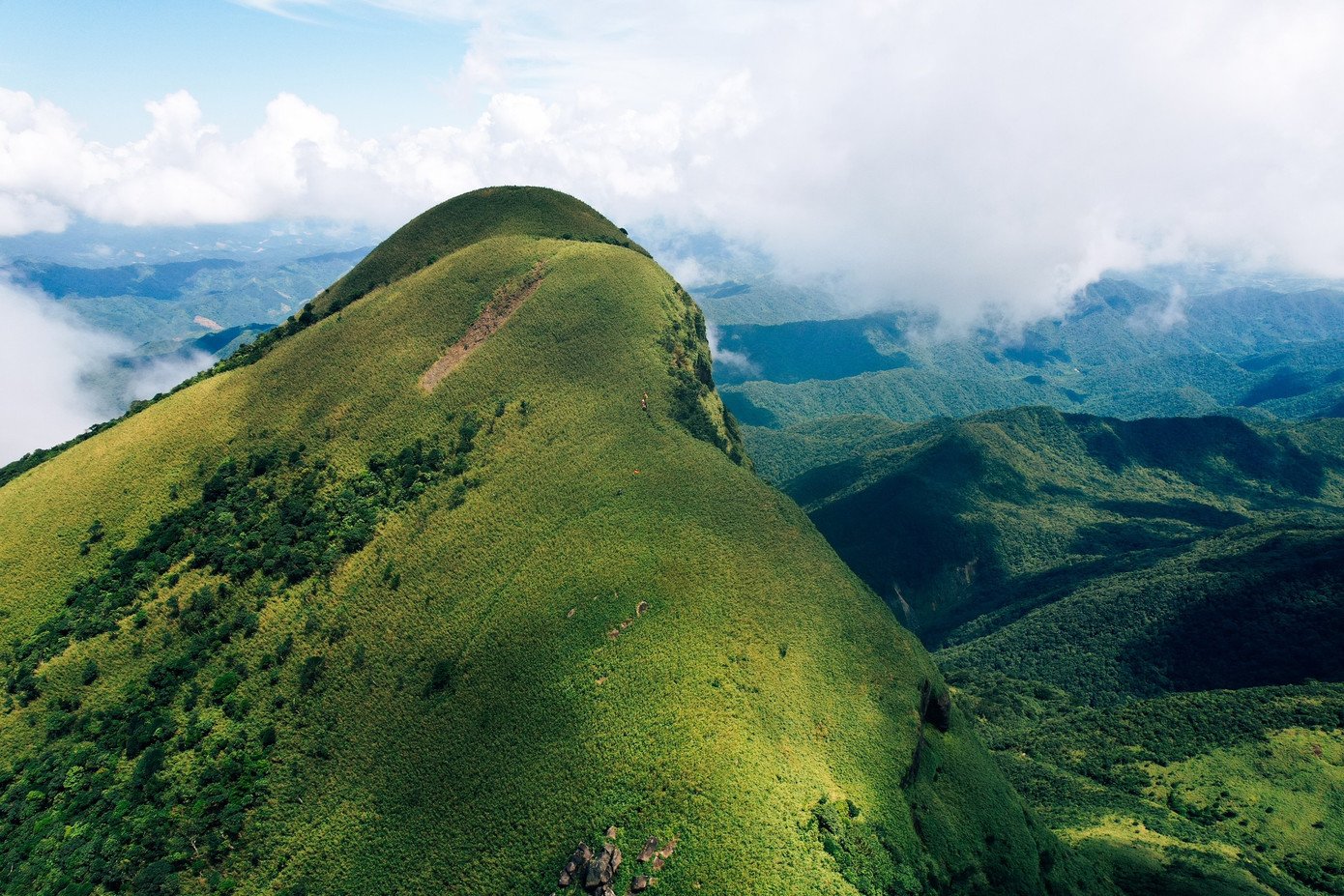 Từ trên đỉnh nhìn xuống, những cánh rừng nguyên sinh trải dài bất tận, thấp thoáng phía xa là dấu hiệu của sự sống mới - những bản làng, những cánh đồng điện gió đang vươn mình trong sương. Đó là bức tranh giao hòa giữa thiên nhiên hoang sơ và nhịp sống con người, vừa yên bình, vừa giàu hy vọng. Giữa thiên nhiên mênh mang ấy, “nóc nhà” Quảng Trị không chỉ như một đỉnh núi cần chinh phục, mà như một không gian để con người tạm dừng, chiêm nghiệm và yêu thêm đại ngàn Trường Sơn.