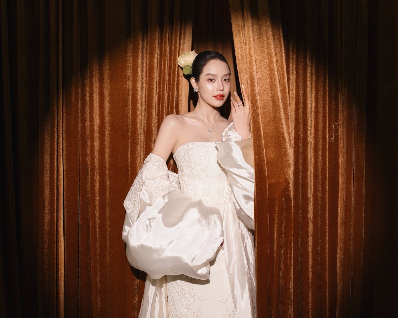 Thiết kế đi kèm áo choàng lộng lẫy với họa tiết sen được in nổi một cách tinh tế trên nền vải trắng. Thanh Thủy cũng sử dụng hoa sen trắng như phụ kiện cài đầu để tôn lên vẻ đẹp tinh khiết, thanh lịch.