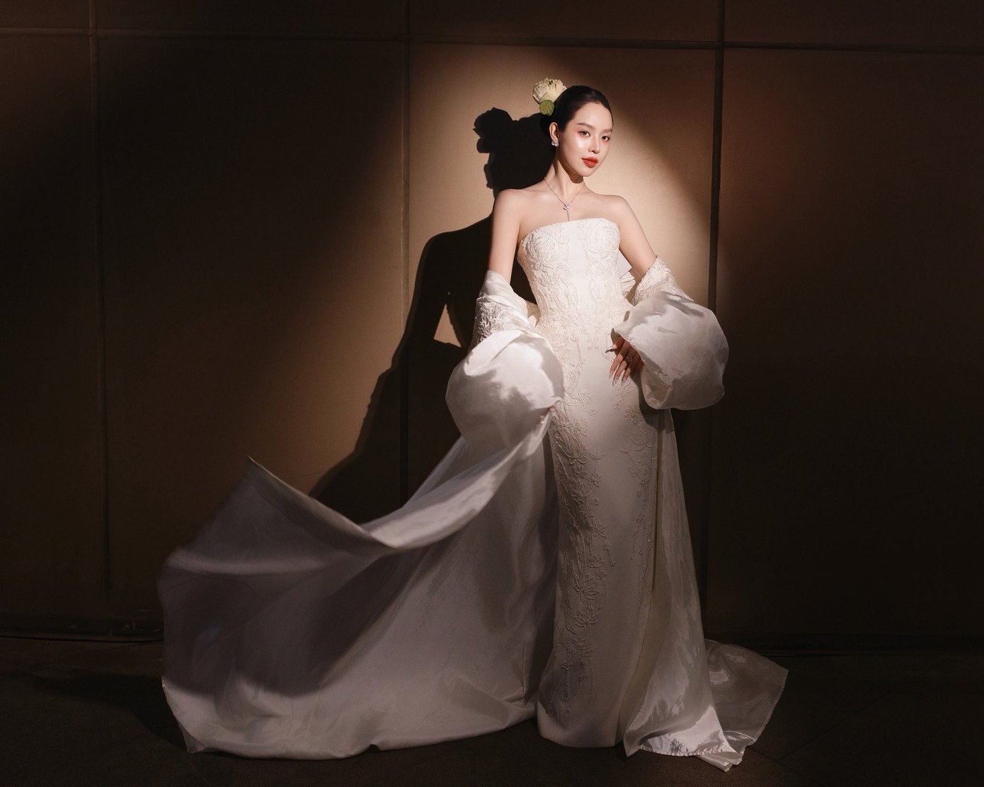 Thiết kế đi kèm áo choàng lộng lẫy với họa tiết sen được in nổi một cách tinh tế trên nền vải trắng. Thanh Thủy cũng sử dụng hoa sen trắng như phụ kiện cài đầu để tôn lên vẻ đẹp tinh khiết, thanh lịch.