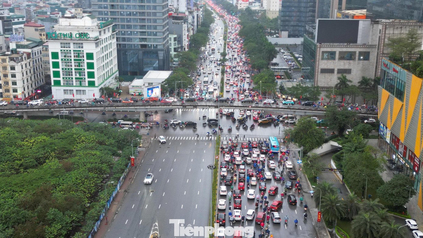 Tại ngã tư Nguyễn Chánh – Trần Duy Hưng, xe máy, ôtô chen chúc, nhích từng chút qua nút giao đông đúc. Người đi đường khoác áo mưa dày, cúi đầu tránh gió, kiên nhẫn chờ đợi giữa dòng xe ken đặc.