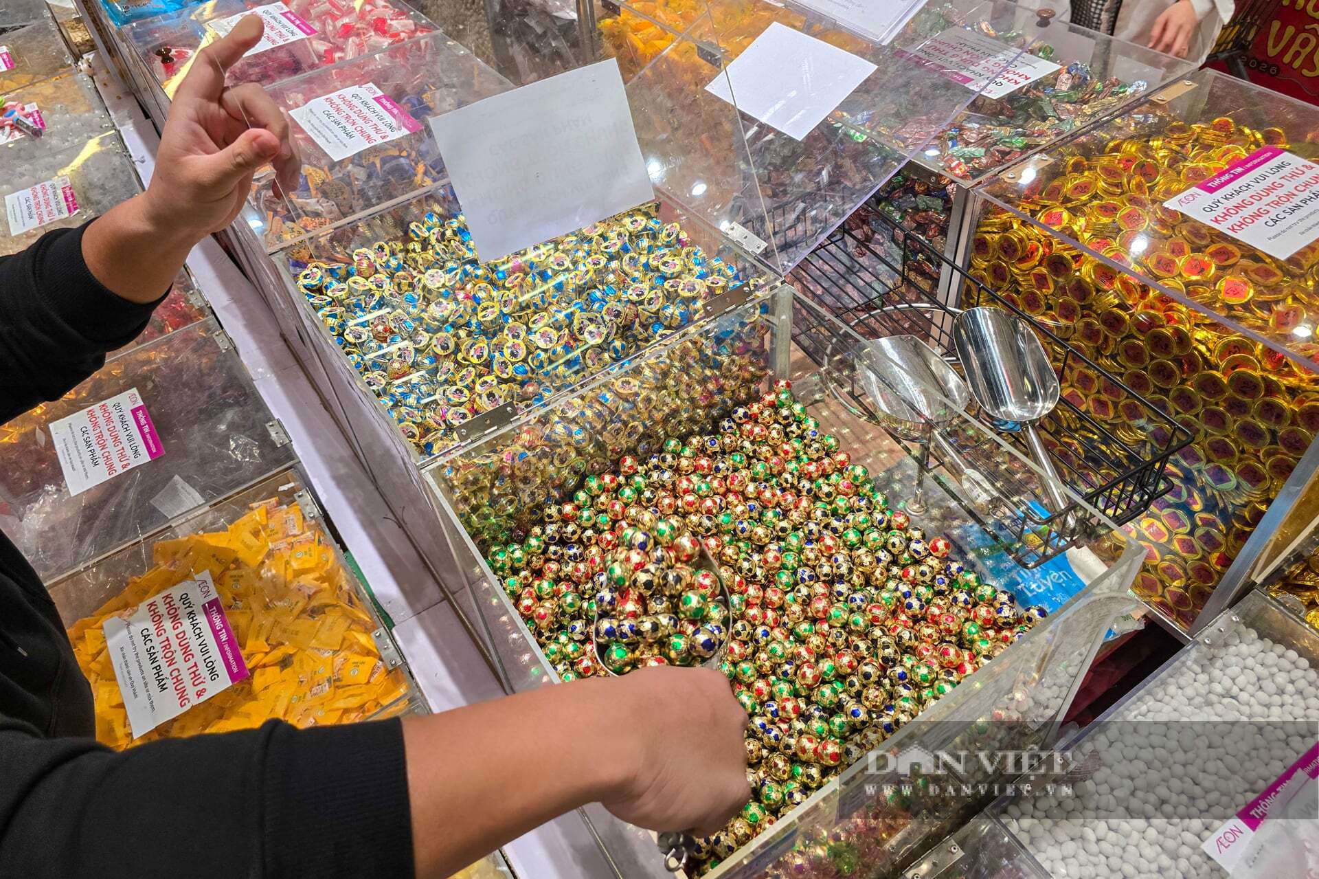 Tại đây, hàng trăm khay bánh, kẹo dẻo, thạch rau câu, sô-cô-la đồng tiền... đủ màu sắc sặc sỡ được đổ đống tạo nên một "ma trận" ngọt ngào vô cùng bắt mắt. Điểm cộng lớn nhất của loại mặt hàng này là mức giá "siêu mềm", chỉ dao động từ 40.000 – 90.000 đồng/kg tùy loại.&nbsp;Tay nhanh thoăn thoắt xúc đầy một túi lớn gồm đủ loại kẹo dẻo và thạch, bà Nguyễn Thị Lan (Thanh Xuân) chia sẻ: "Tết nhất chủ yếu mua cho trẻ con đến chơi hoặc bày khay mứt cho đẹp. Kinh tế năm nay khó khăn, mua bánh hộp nhập khẩu thì tốn kém quá, lại được ít. Cứ mua hàng cân thế này vừa rẻ, vừa chọn được nhiều vị, bày ra khay trông rất đầy đặn và rực rỡ".