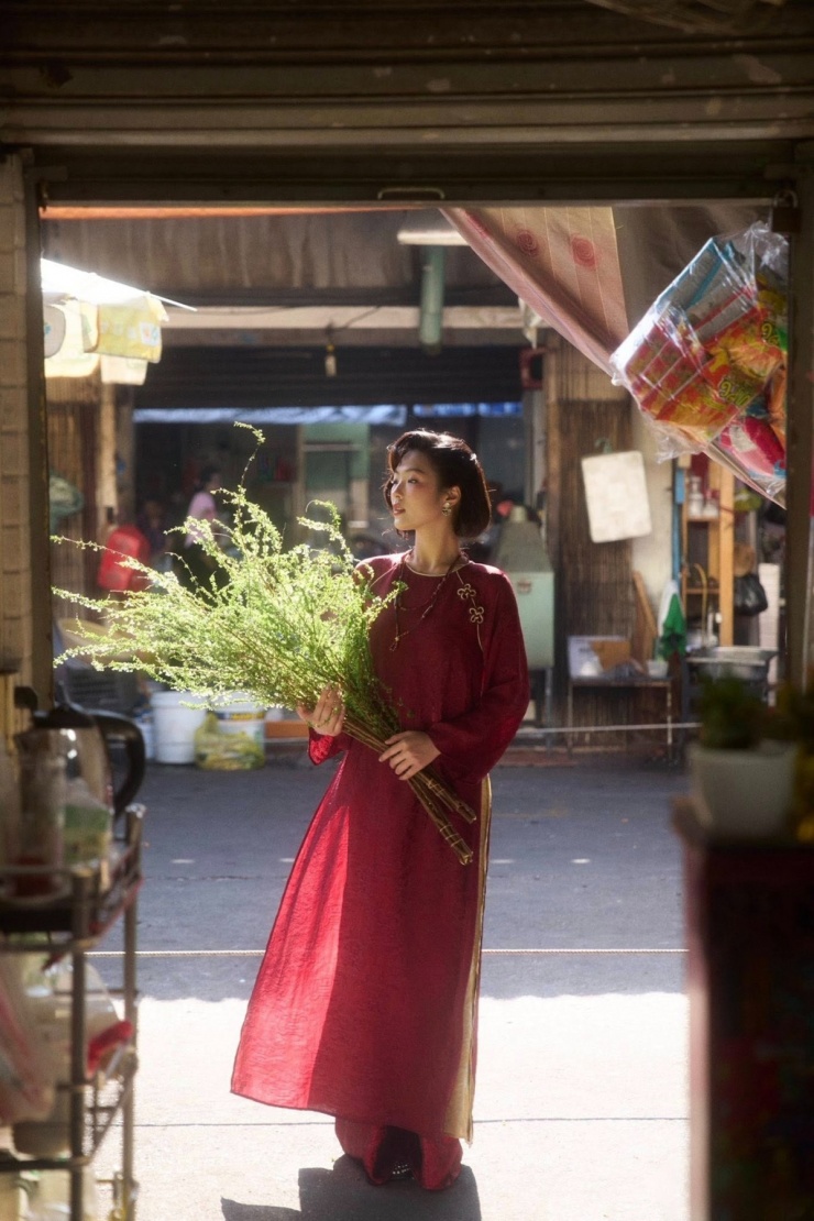 Một cô gái hướng đến hình ảnh Tết xưa với kiểu tóc uốn nếp cổ điển của thập niên 1960-1970, áo dài đỏ, tay cầm cành tuyết mai.