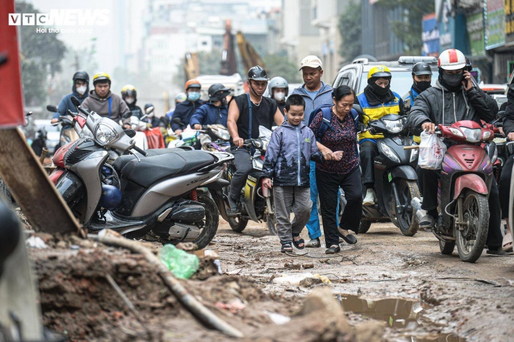 Hai bên tuyến đường tập trung nhiều chung cư và trường học nên lưu lượng người qua lại luôn đông. Trong điều kiện mặt đường lầy lội, nhiều phụ huynh phải dắt tay hoặc bế con qua đoạn bùn để vào trường.