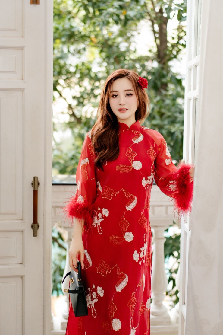 Vy Oanh rạng rỡ khi khoác lên mình tà áo dài sắc đỏ thắm, biểu tượng của sự may mắn và hạnh phúc. Bộ trang phục nổi bật với những đóa hoa trắng được thêu tỉ mỉ dọc thân áo trên nền vải gấm cao cấp, tạo nên nét thanh lịch và quý phái.