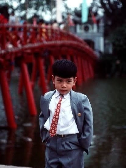 Một cậu bé ăn mặc chỉn chu, đứng tạo dáng bên cầu Thê Húc.