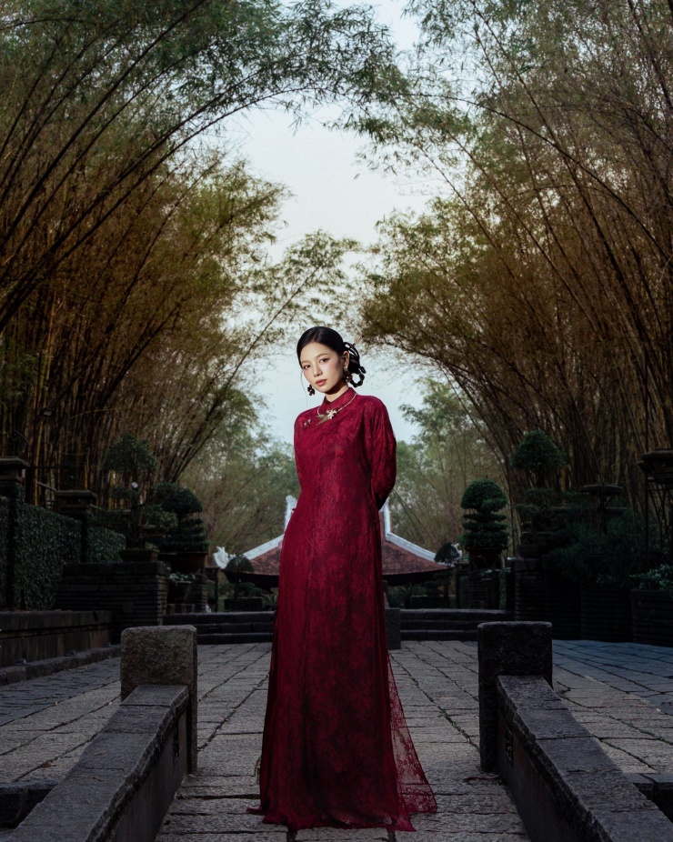 Bức ảnh thể hiện vẻ đẹp thanh thoát và trang nhã của tà áo dài đỏ thắm, nổi bật giữa không gian thiên nhiên. Chiếc áo dài ren tinh tế mang đến sự hòa quyện hoàn hảo giữa nét truyền thống và hiện đại, tôn lên vẻ duyên dáng, kiêu sa của người mặc.