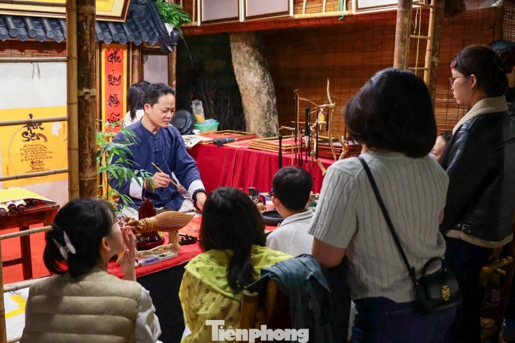 Nhiều gia đình, nhóm bạn trẻ xếp hàng chờ đến lượt trong tiết trời se lạnh. Dưới những mái lều đỏ, các ông đồ trong áo dài truyền thống chăm chú viết thư pháp, từng nét bút chậm rãi trên nền giấy dó.